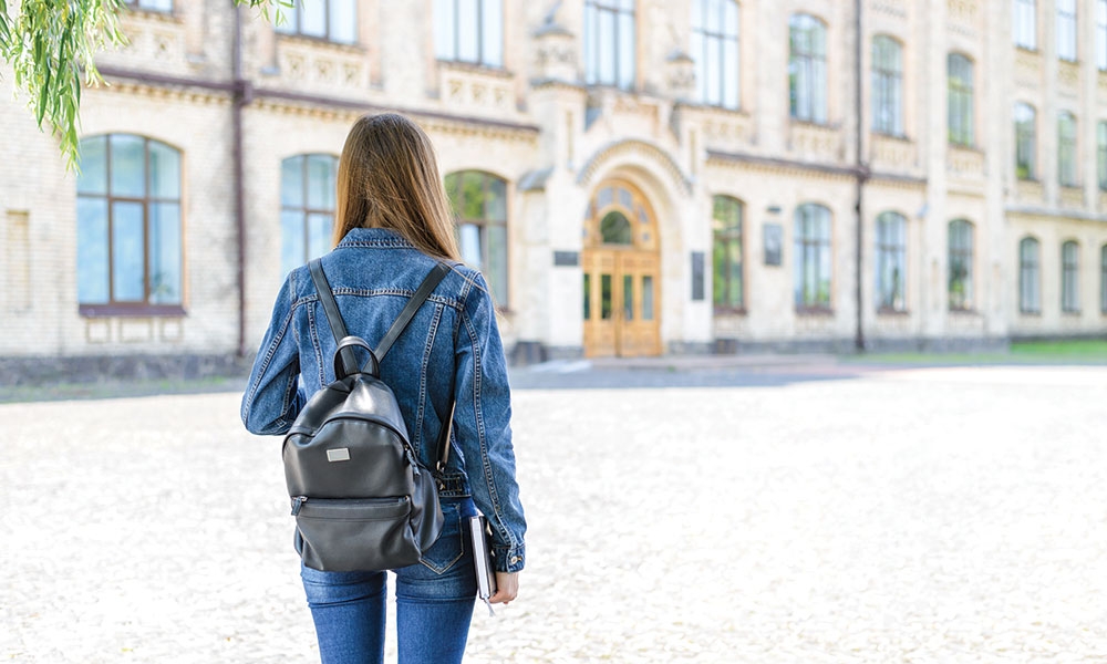 Young woman wearing a backpack facing a school