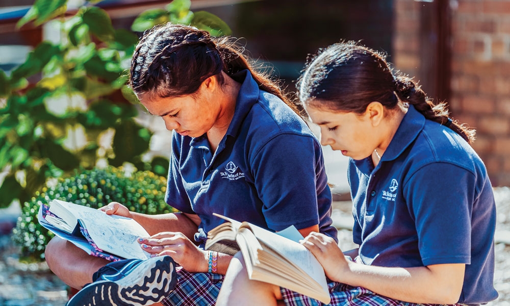 Two Catholic school girls reading books outside