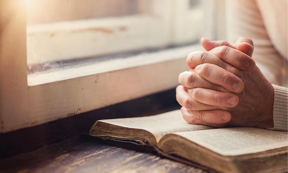 Hands folded in prayer over open Bible