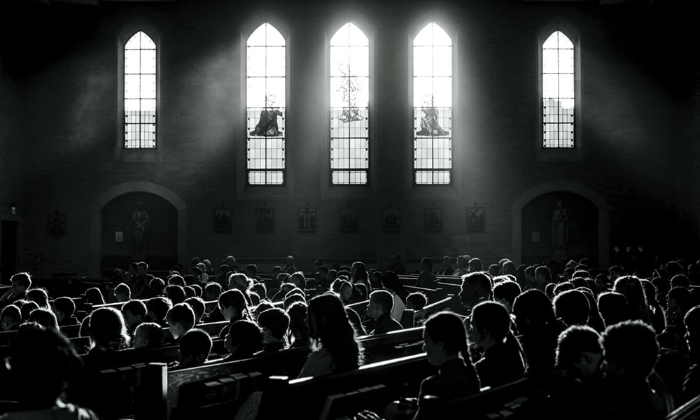 Black and white photo of people sitting in pews inside a church