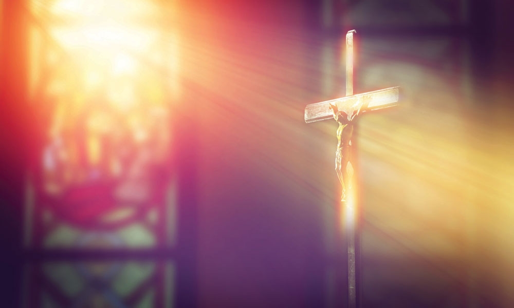 Crucifix illuminated by strong ray of sunshine through a stained glass window