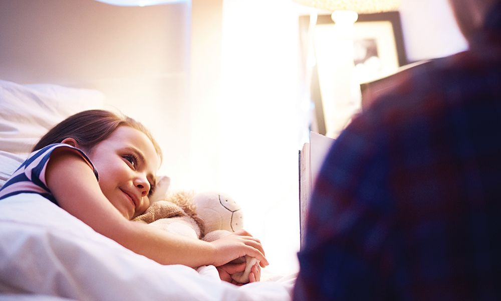 Parent reading child bedtime story in bed